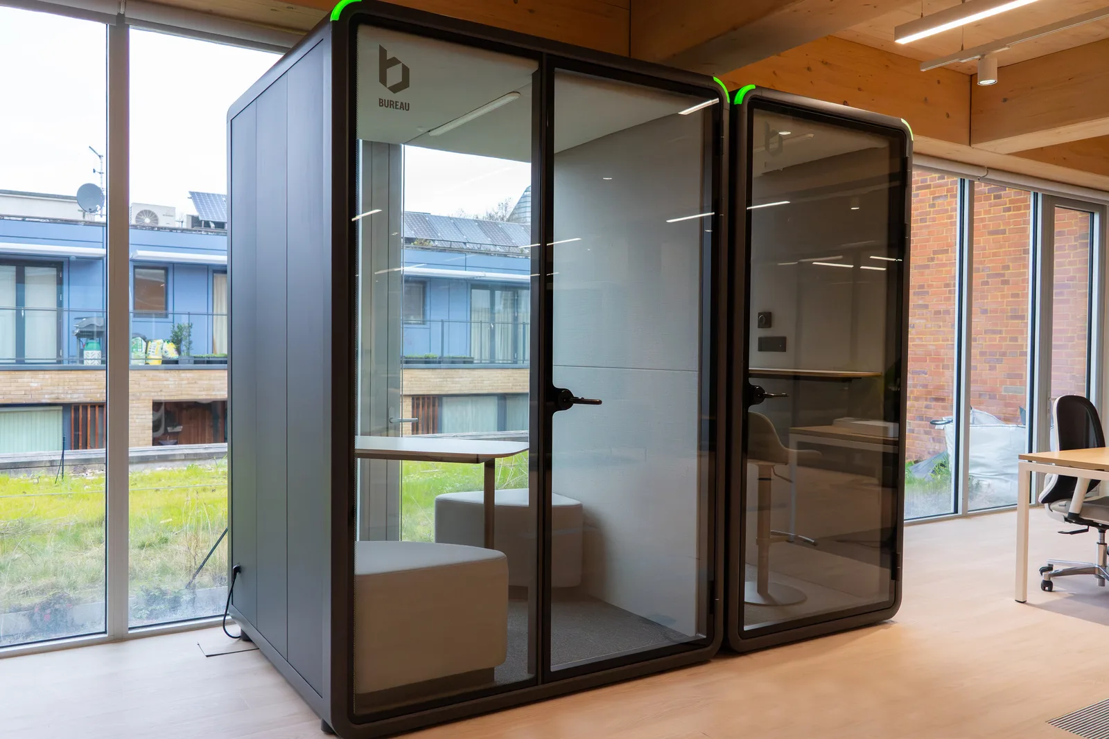 Two Bureau One+ booths installed side by side in a bright modern office with floor-to-ceiling windows